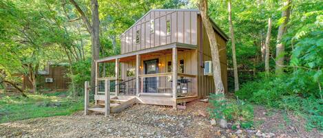 A wooden cabin with a porch, surrounded by trees.