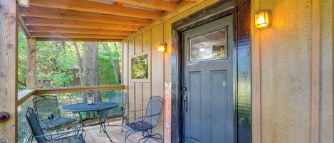 A wooden deck with a black door, two metal chairs, and a table.
