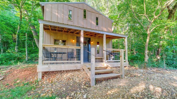 A wooden cabin with a porch, built into a forested area.