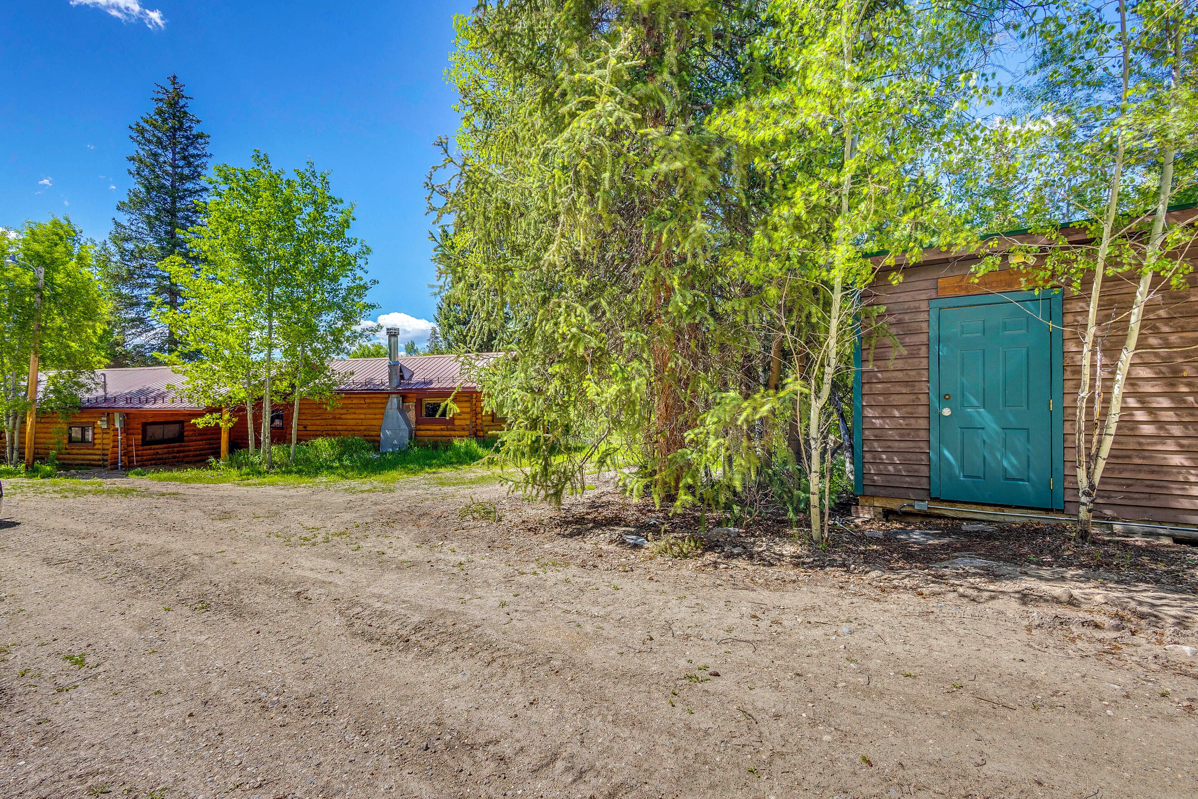 A rustic cabin with a green door, surrounded by trees and a dirt ground.