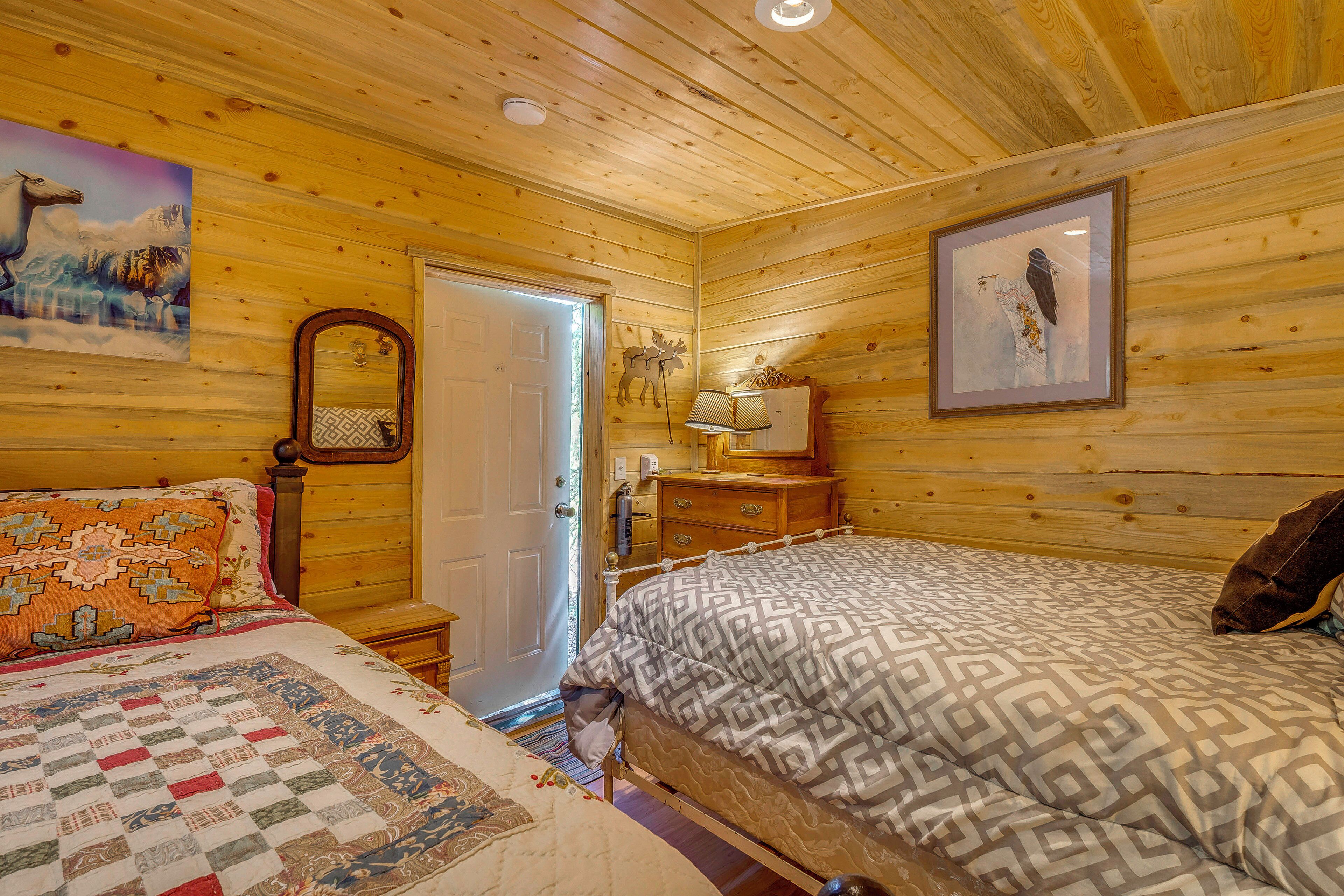 A wooden cabin bedroom with a bed, a dresser, a mirror, and a framed picture on the wall.
