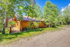 A wooden cabin with a porch, surrounded by trees and a clear sky. - Families w/ Pets! Riverfront Retreat in Grand Lake (Grand Lake)