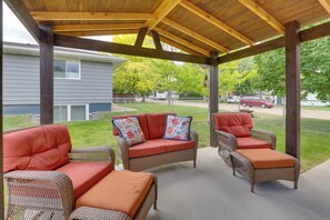 A covered patio with wicker furniture and cushions, a wooden ceiling, and a view of a residential area. - Black Hills Basecamp: Sturgis Home w/ Yard! (Sturgis)