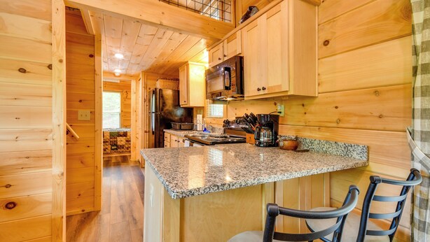 A wooden cabin interior with a kitchen area featuring granite countertops, a microwave, and a coffee maker. There are two chairs at a small table.