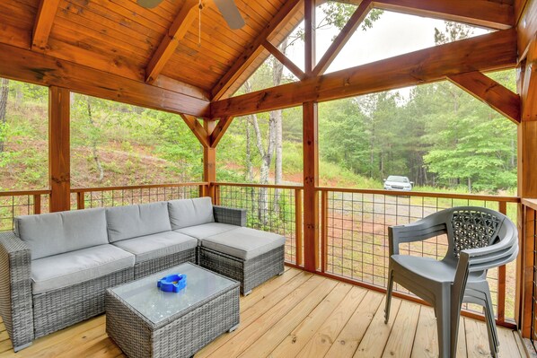 A covered outdoor seating area with a grey sectional sofa, wicker coffee table, and a plastic chair.