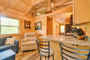 Ein Interieur einer Hütte mit Küche, einem Essbereich mit Bar, einer Couch und einem Sessel.