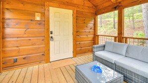 A wooden cabin with a door, a porch, a wicker sofa, and a glass table.