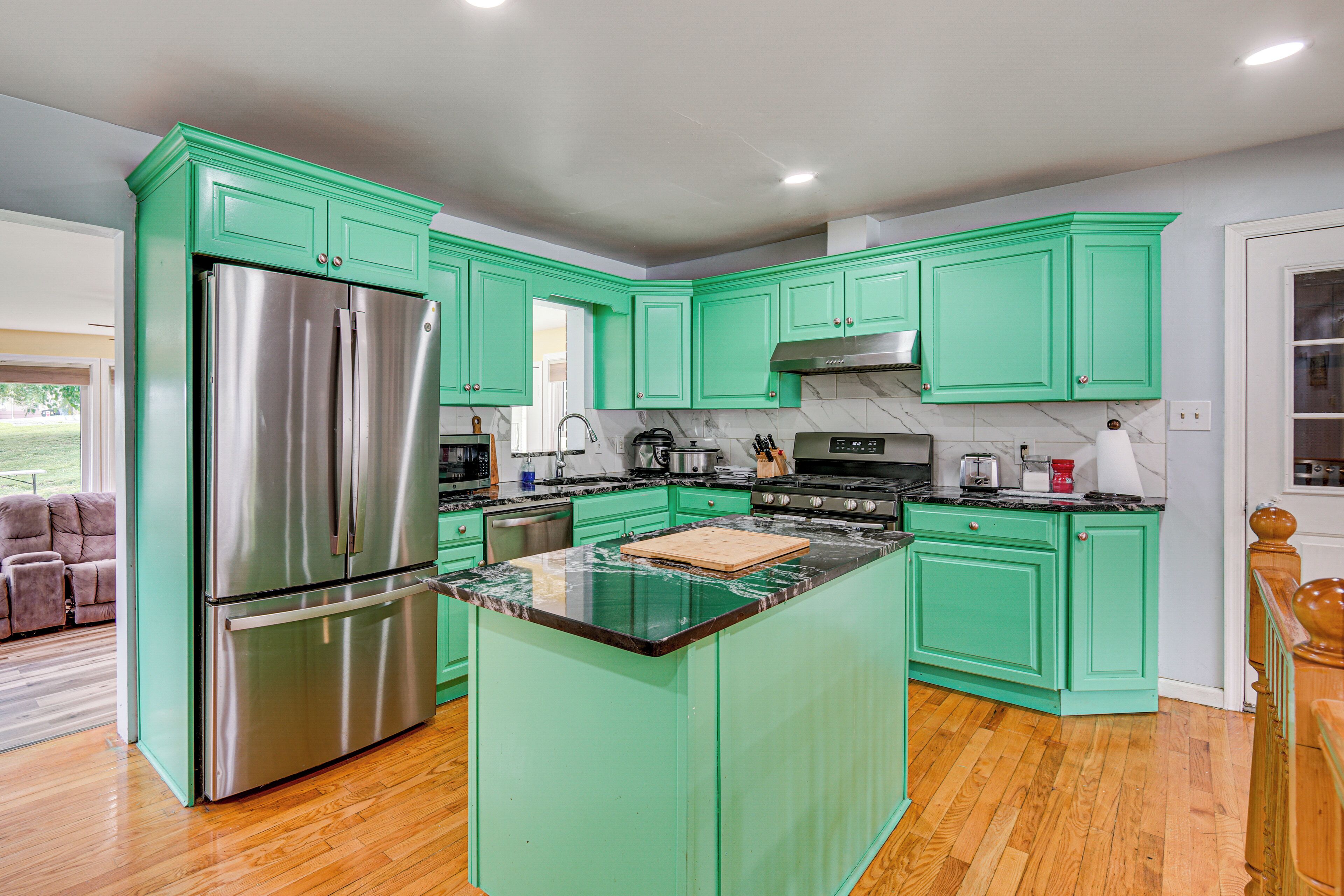 A kitchen with green cabinets, a stainless steel refrigerator, and a marble countertop.