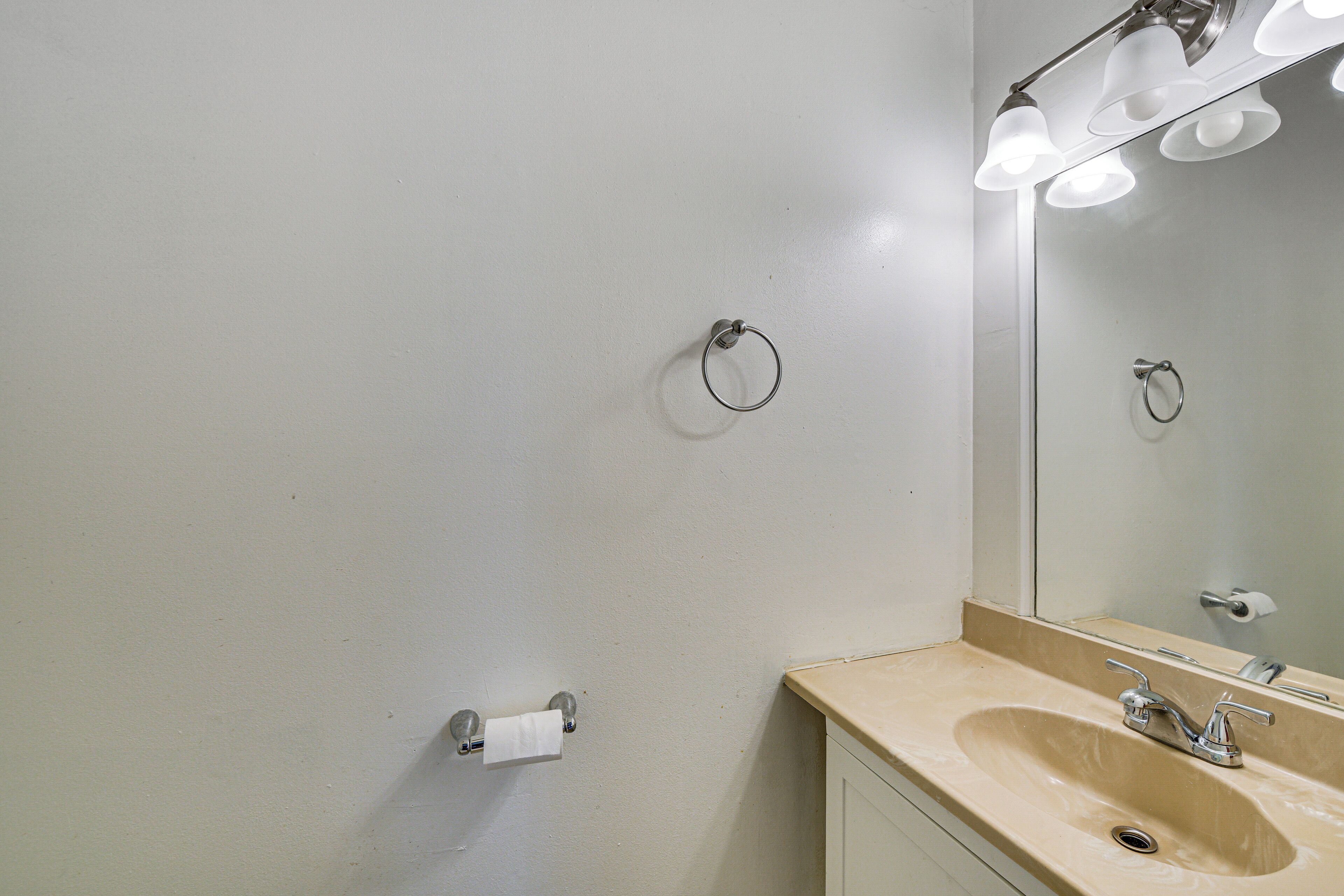 A bathroom with a sink, mirror, towel ring, and toilet paper holder.