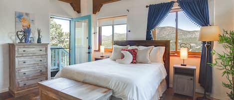 Ein Schlafzimmer mit Bett, Nachttisch, Kommode, Bank, Lampe und Blick ins Freie.