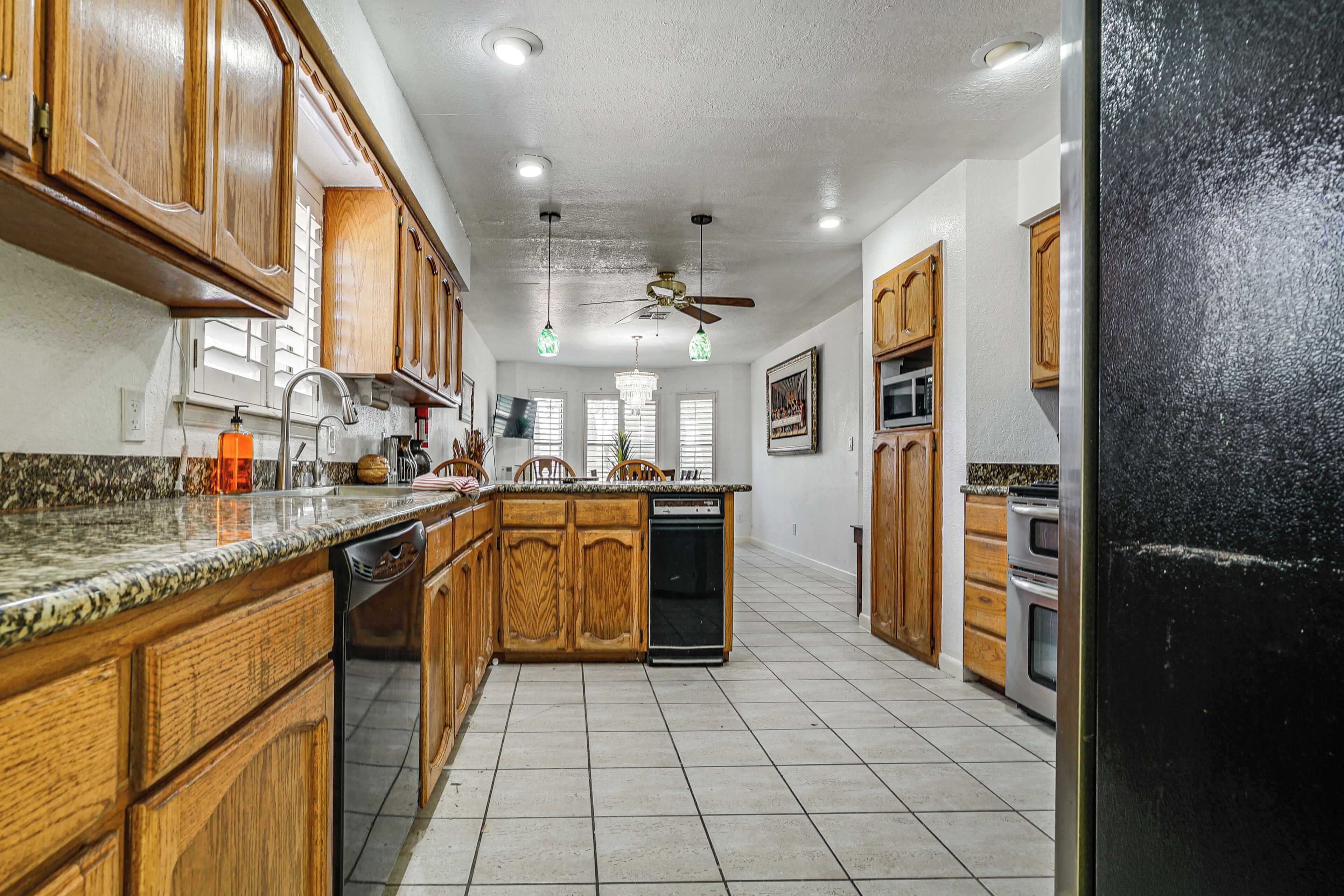 A kitchen with wooden cabinets, granite countertops, a dishwasher, a ceiling fan, and a refrigerator.