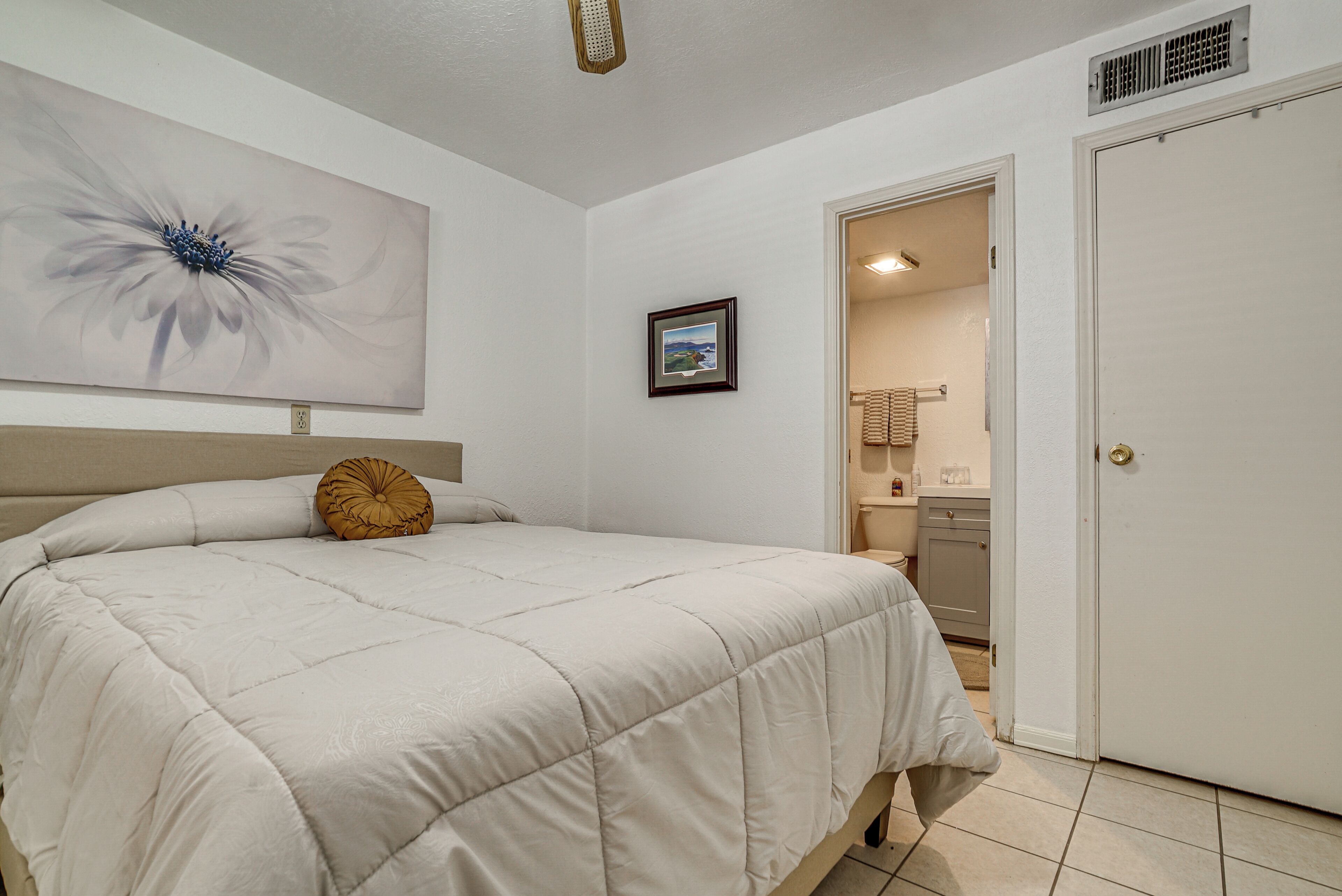 Un dormitorio con una cama, un cuadro en la pared y una puerta que da a un baño.