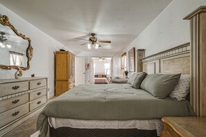 Une chambre à coucher comprenant un lit, une commode, un miroir, un ventilateur de plafond et un couloir menant à une autre pièce.