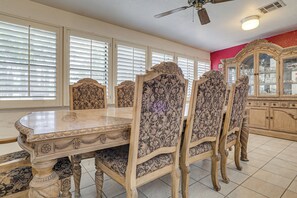 Un coin repas avec une table en marbre et des chaises à motifs floraux, un ventilateur de plafond et un meuble avec des portes en verre.