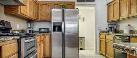 A kitchen with wooden cabinets, stainless steel appliances, granite countertops, and a tiled floor.