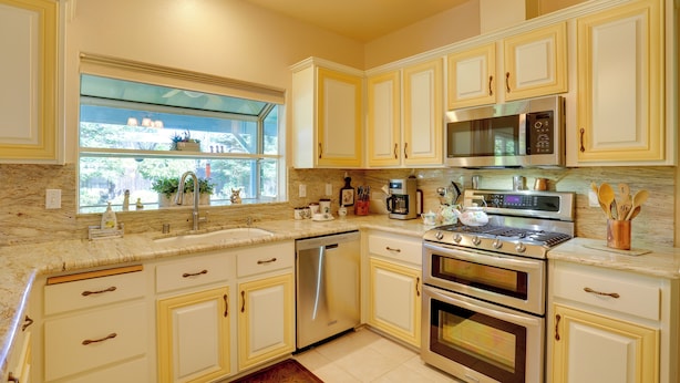 A kitchen with white cabinets, a stainless steel dishwasher, a double oven, a microwave, and a window with a view of greenery. - 5 Mi to Sundial Bridge & River! Pet-friendly Haven (Redding)