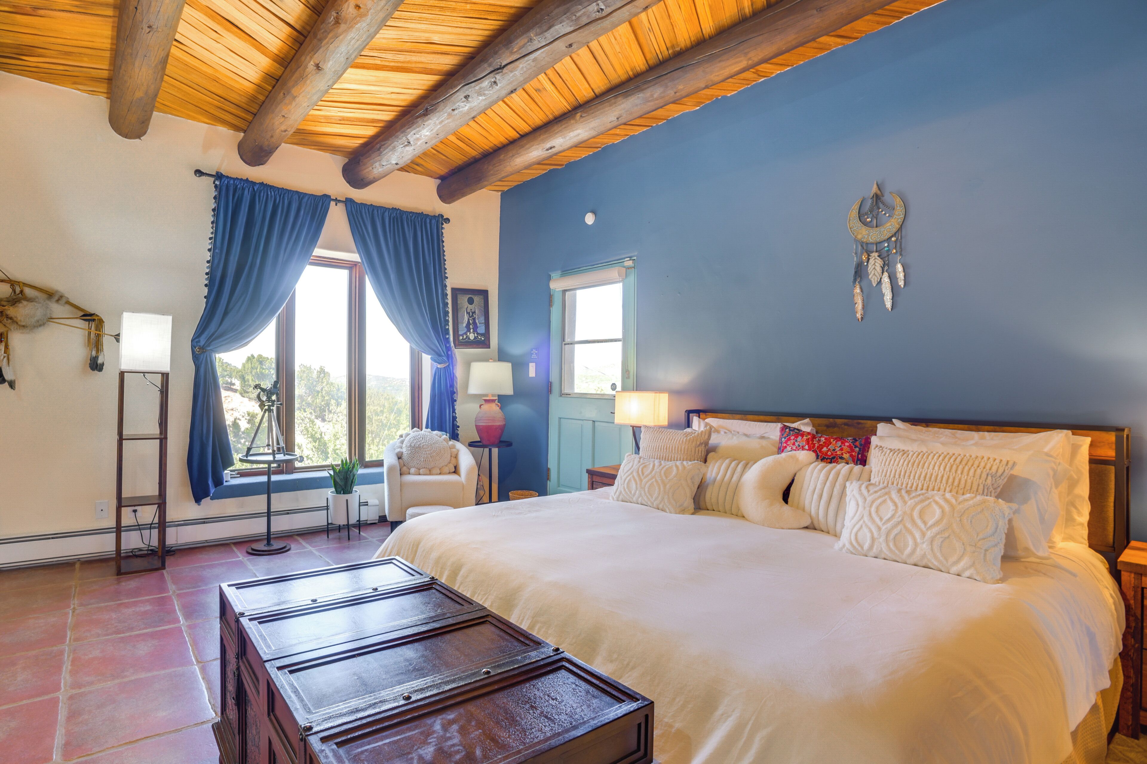 Un dormitorio con una cama grande, techo de madera, ventana con cortinas, una lámpara de noche y un adorno en la pared.