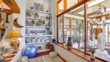 A cozy room with a large window, wooden beams, shelves with decorative items, a blue exercise ball, and a sign that reads 'THIS FAMILY IS.'
