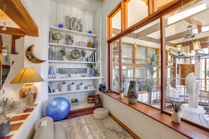 A cozy room with a large window, wooden beams, shelves with decorative items, a blue exercise ball, and a sign that reads 'THIS FAMILY IS.' - Luxurious Retreat w/ Stunning Views in Santa Fe (Santa Fe)