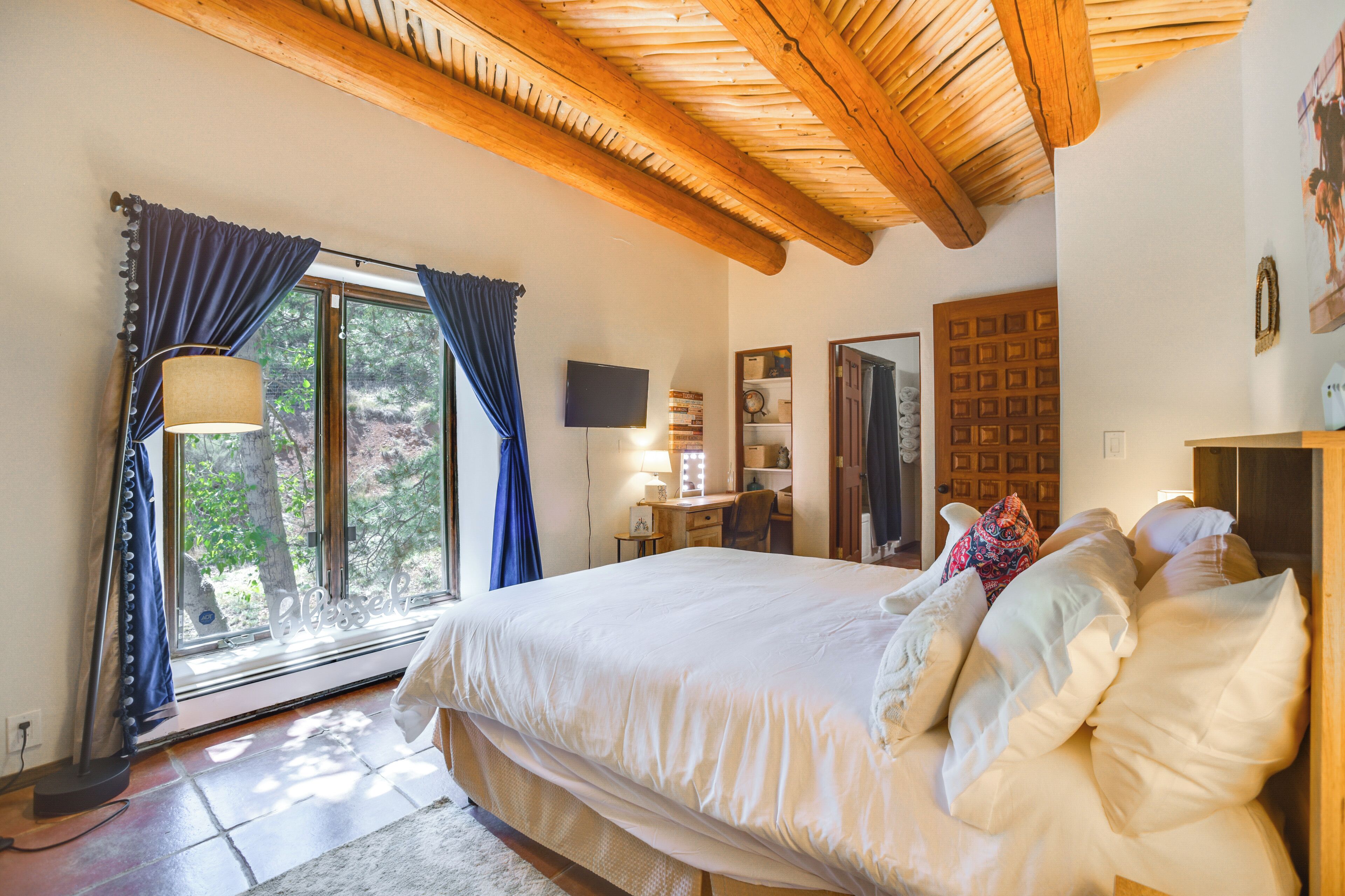 Un dormitorio con una cama grande, un escritorio, una silla, un televisor y una ventana con cortinas.