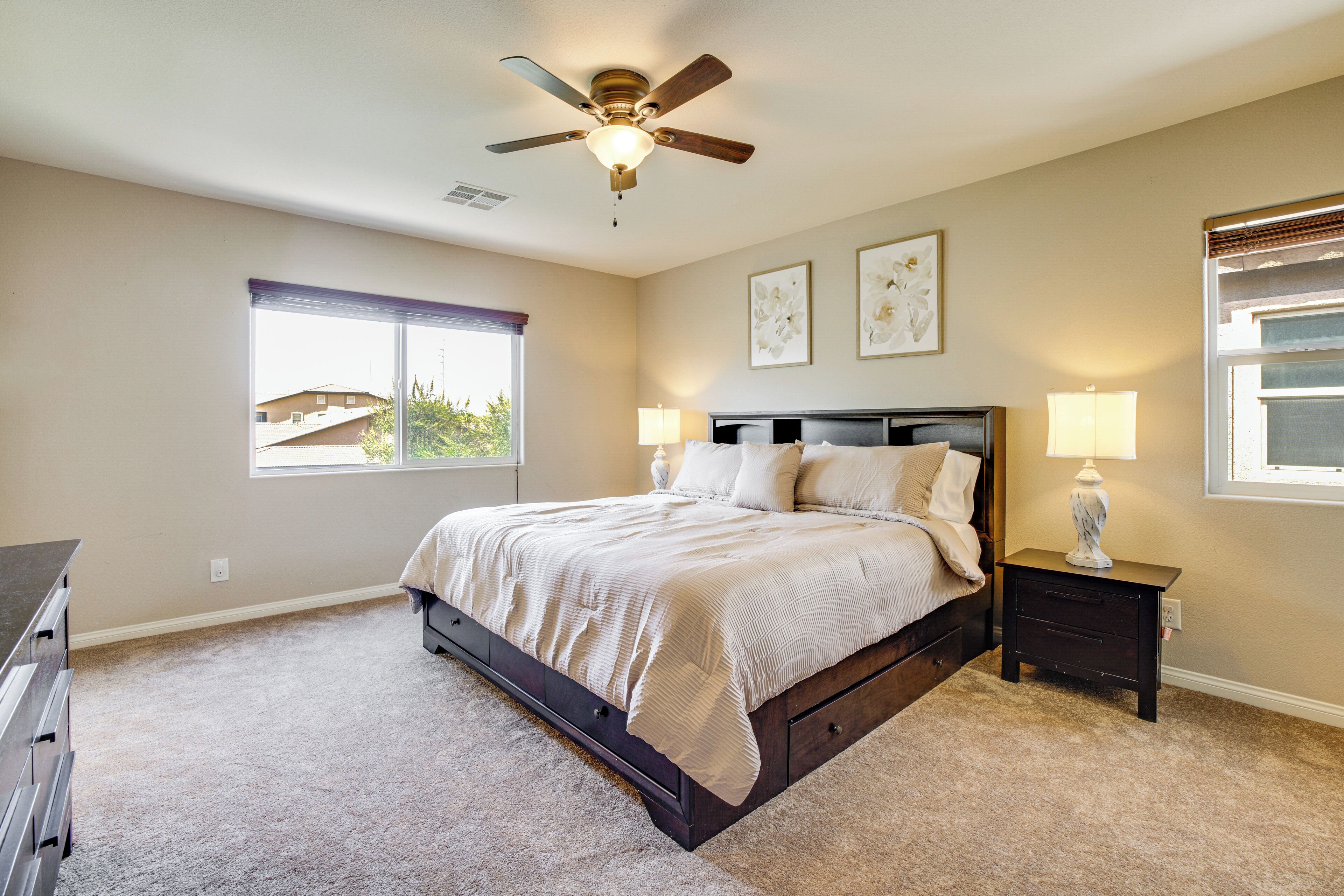 A bedroom with a bed, a ceiling fan, a window, and a nightstand with a lamp.