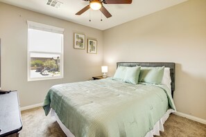 A bedroom with a bed, a ceiling fan, a window, and a nightstand with a lamp.