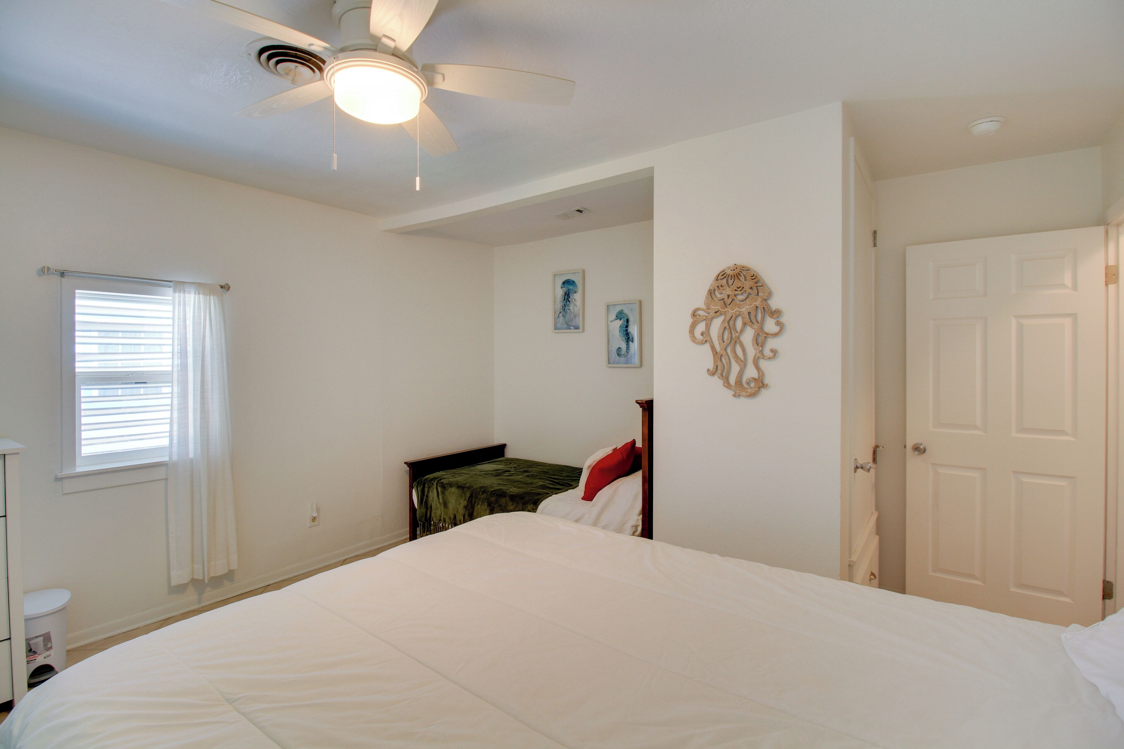 A bedroom with a bed, a ceiling fan, a window with blinds, and a door.