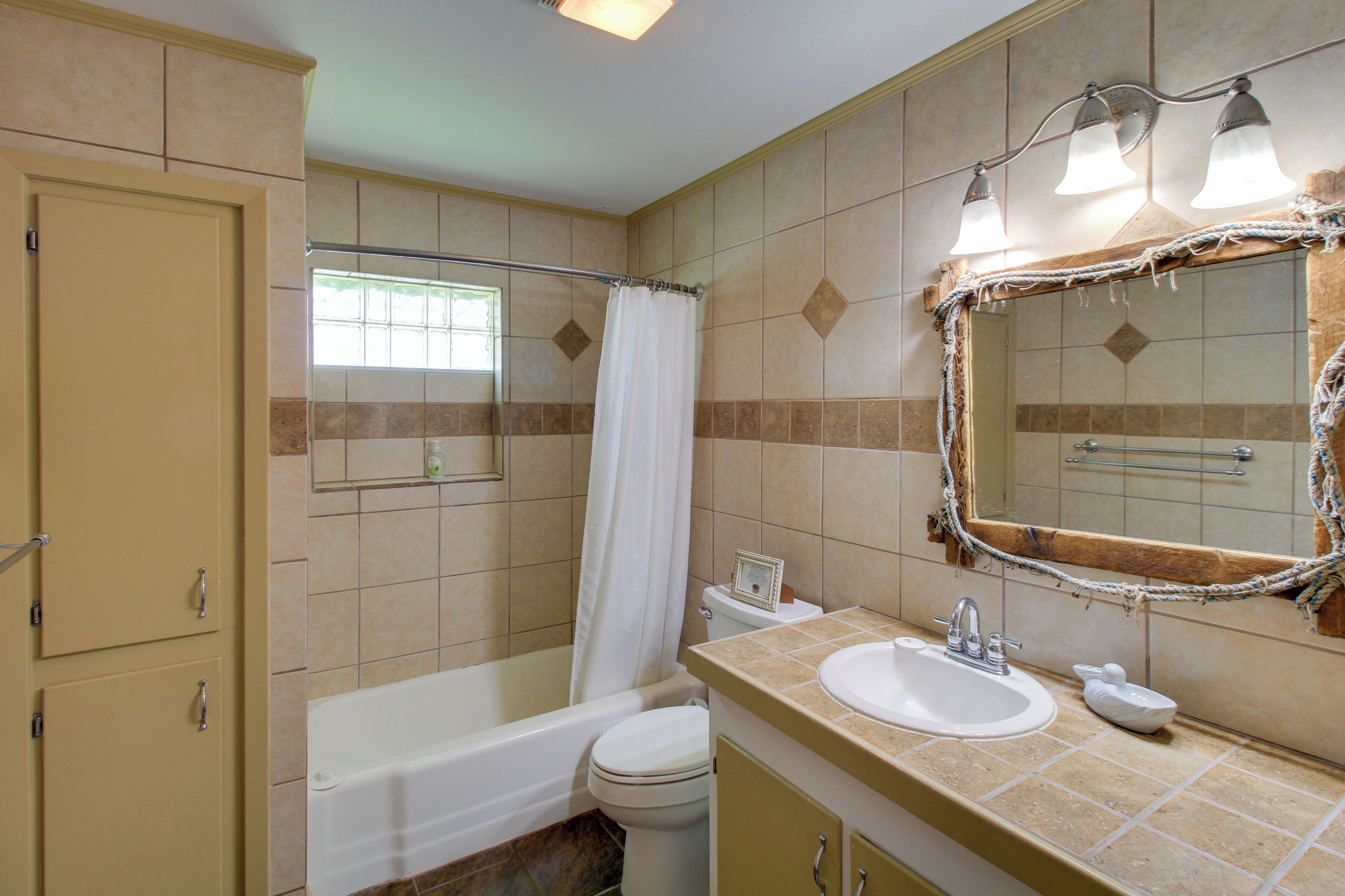 A bathroom with a bathtub, toilet, sink, and a mirror with lights.