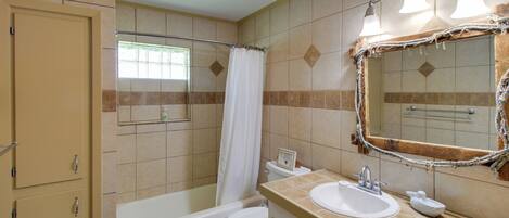 A bathroom with a bathtub, toilet, sink, and a mirror with lights.