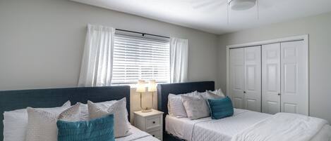 A bedroom with two beds, a nightstand with a lamp, a window with curtains, and a closet.