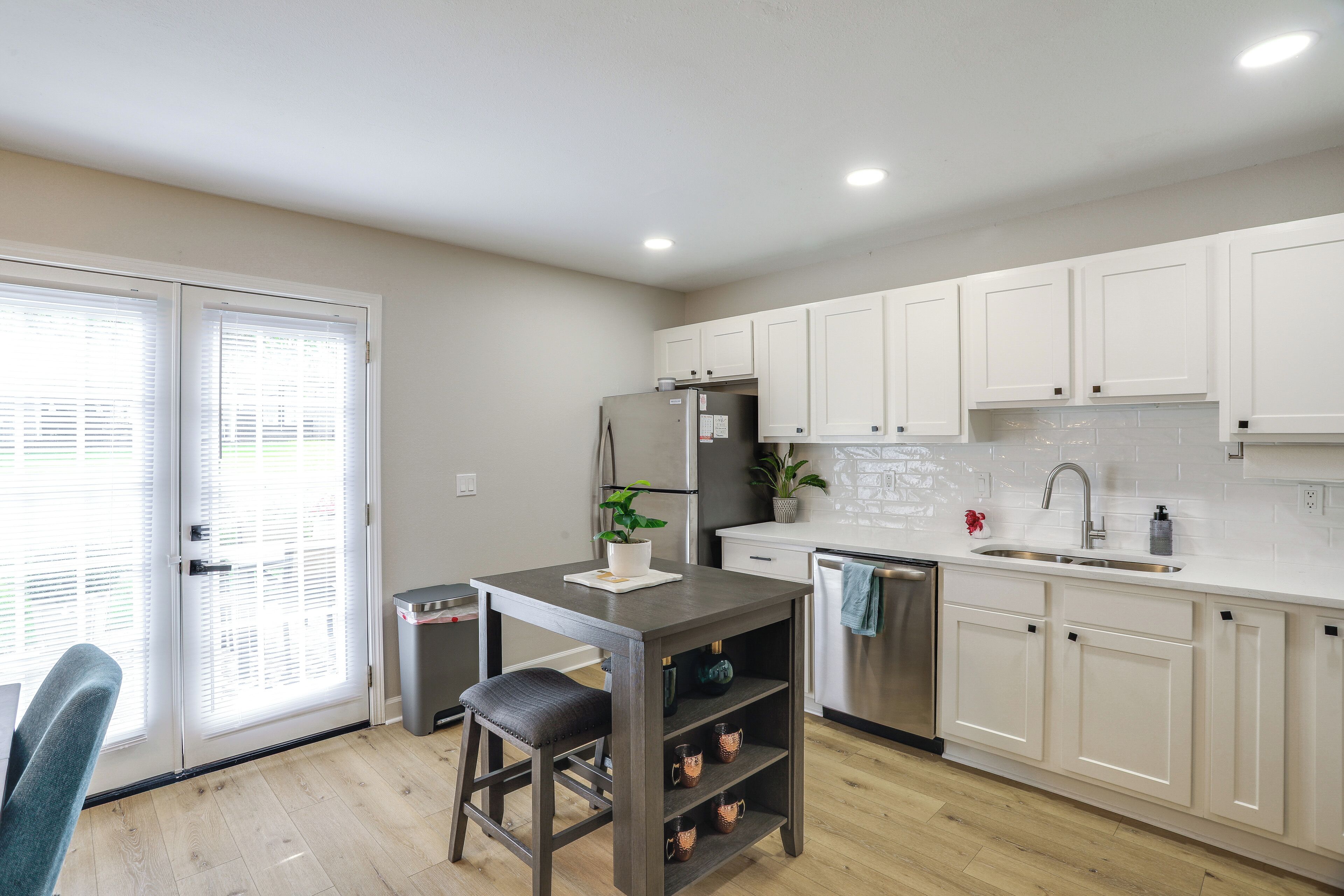 A modern kitchen with white cabinets, a stainless steel refrigerator, a sink, and a dining area with a table and chair.