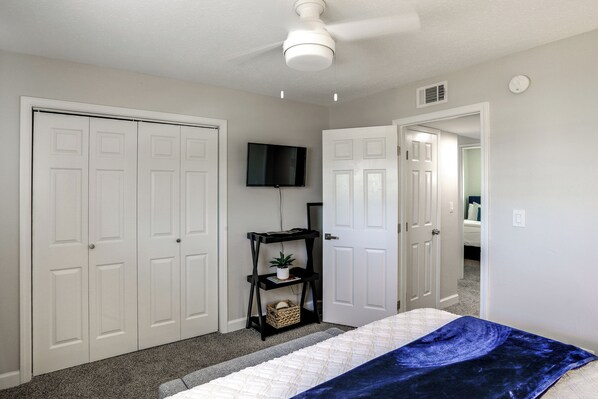 A bedroom with a bed, a ceiling fan, a TV, and a door leading to another room.