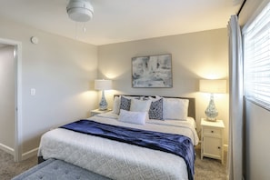 A bedroom with a bed, bedside lamps, a ceiling fan, a painting, and a window with curtains. - Walk to Stadium and Campus! Cozy Townhome w/ Pool (Oxford)