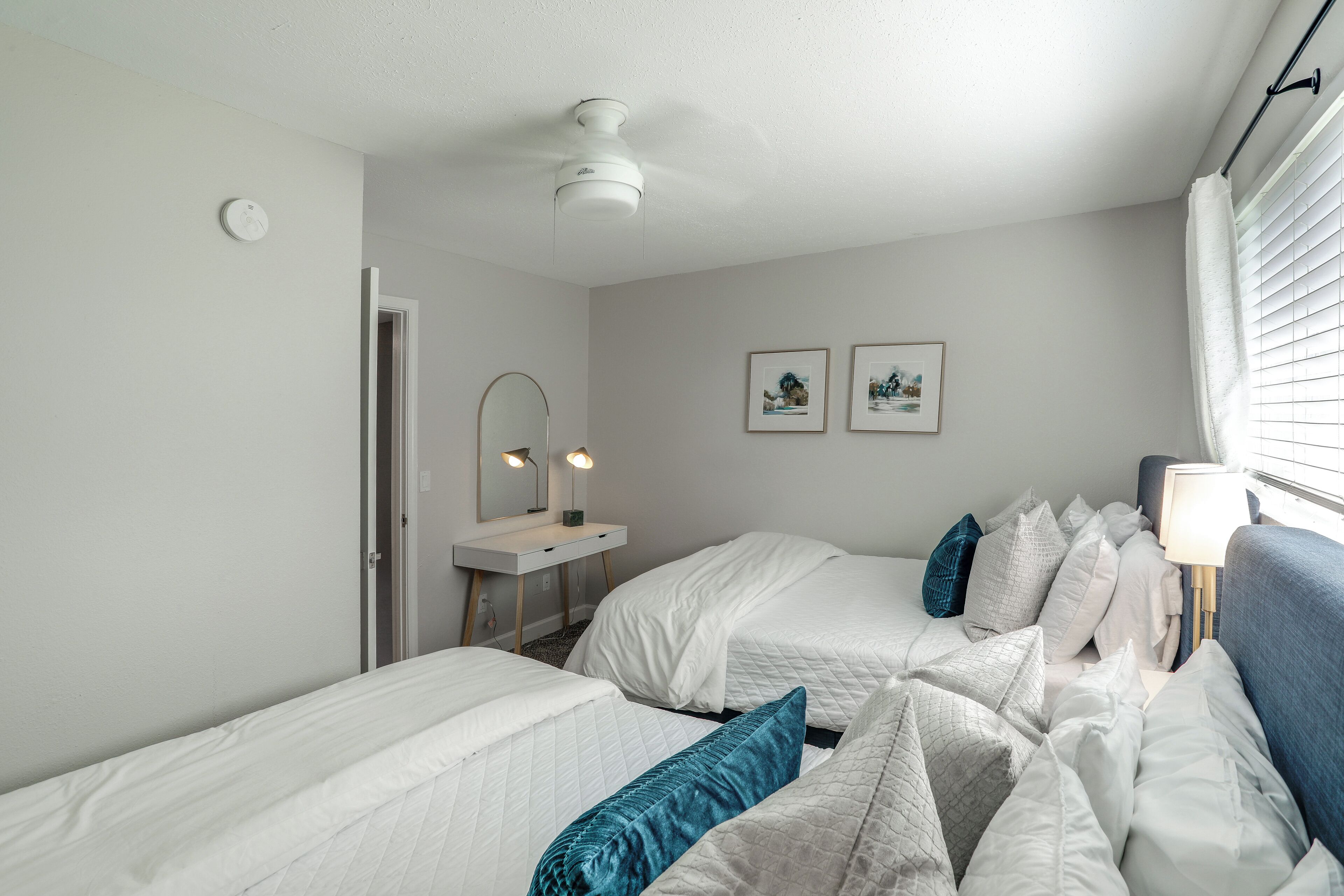 Ein Schlafzimmer mit zwei Betten, einem Nachttisch mit Lampe, einem Deckenventilator und zwei gerahmten Bildern an der Wand.