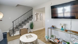 Un salon avec un escalier, un téléviseur à écran plat, une table basse ronde et une console sur laquelle sont disposés des objets décoratifs.