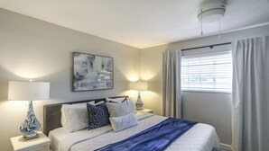 Une chambre à coucher avec un lit, des tables de chevet, des lampes, un tableau et une fenêtre avec des rideaux.