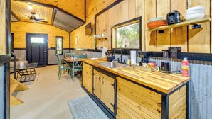 A wooden interior with a kitchen area, including a sink, cabinets, and a dining table with chairs. - Wren's Nest Cabin: Missouri Ozarks Getaway! (Stella)