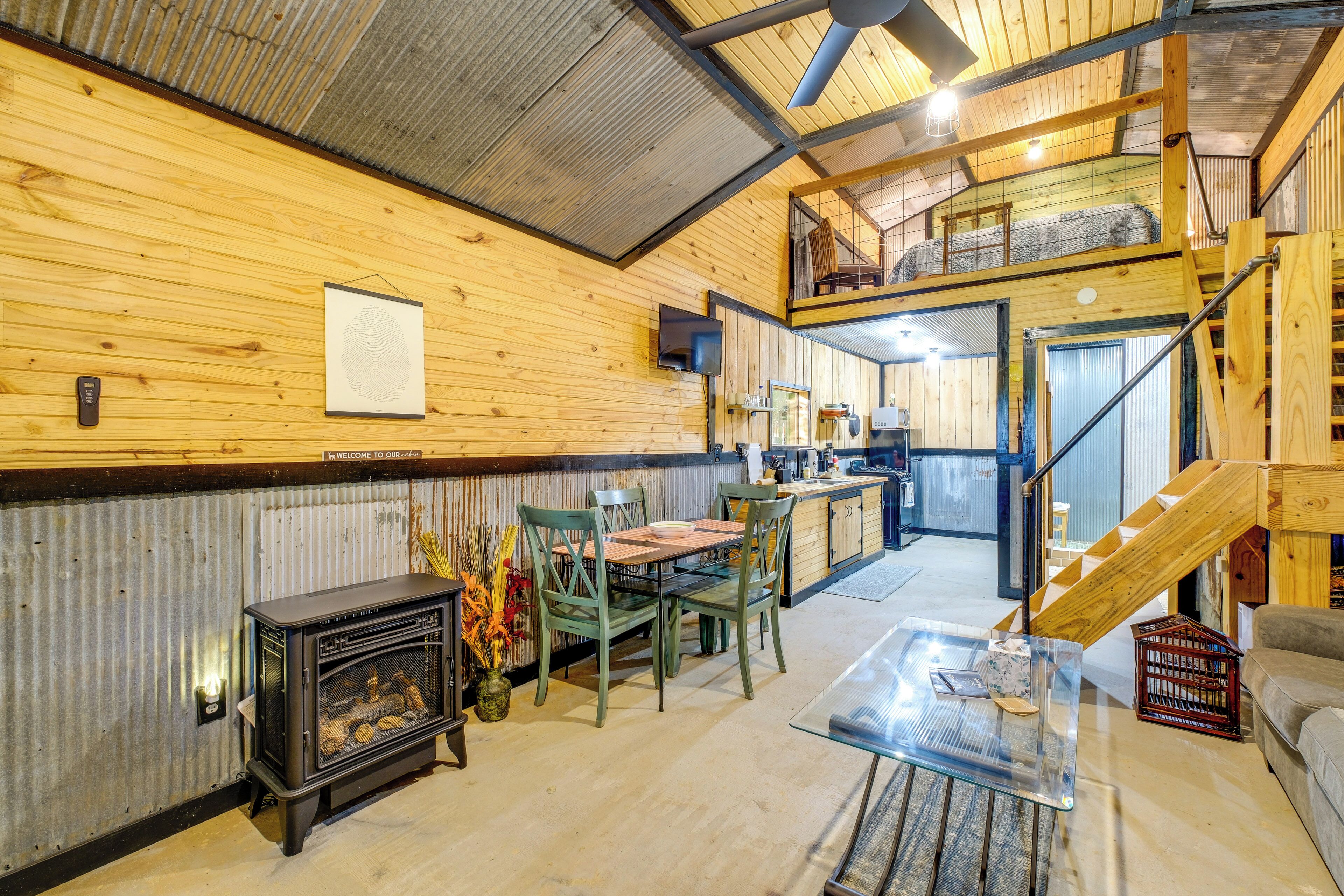 A cozy interior with a wooden wall, a fireplace, a dining area, and a staircase leading to an upper level.