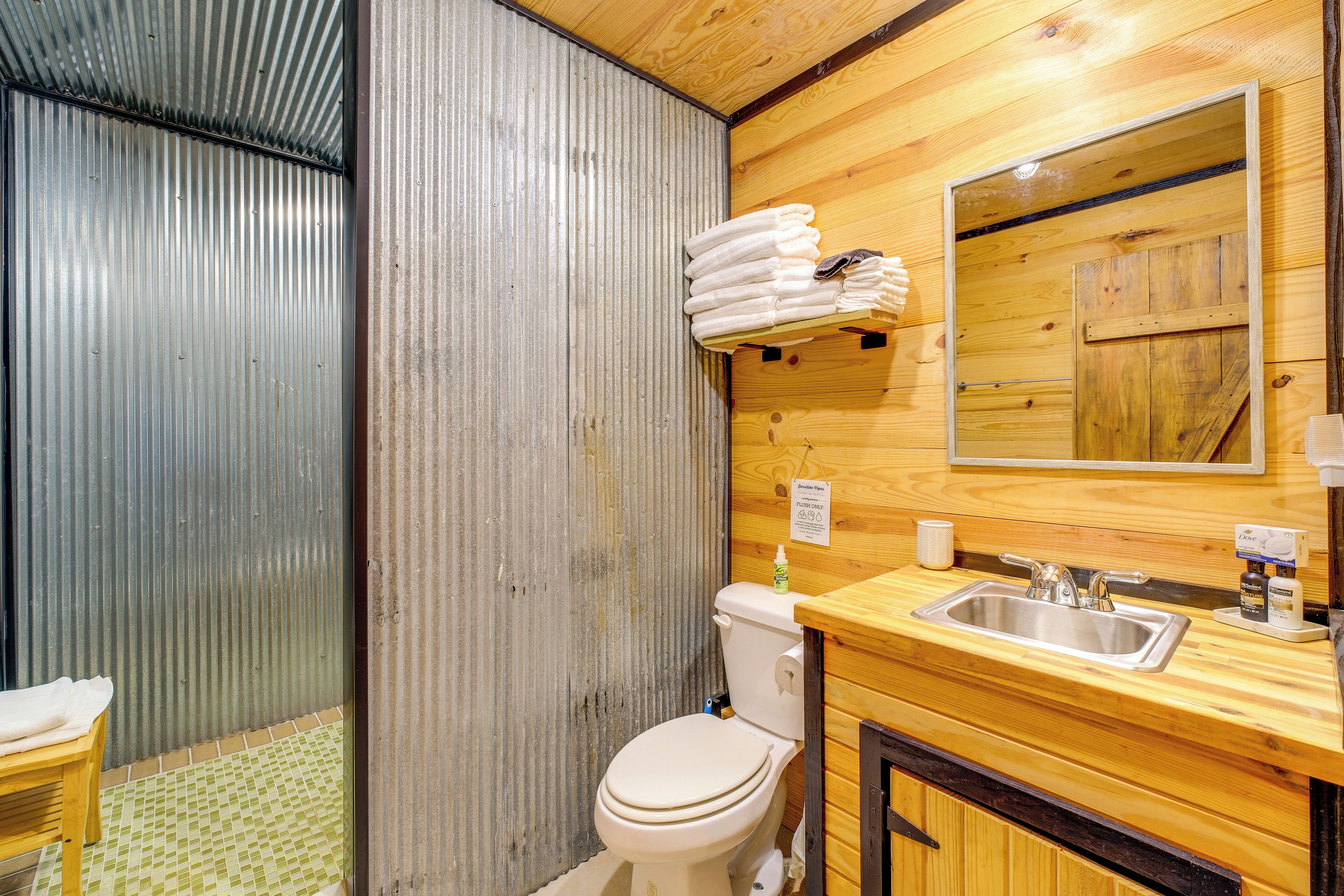 A bathroom with a toilet, sink, mirror, and wooden walls.