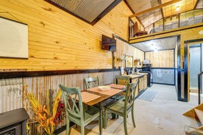 A cabin interior with a dining table, chairs, a kitchen area, and a loft space. - Fish, Hike & Unwind! Rustic Ozark Cabin (Stella)