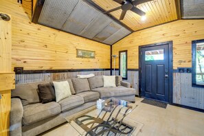 A wooden interior with a sofa, a glass coffee table, a ceiling fan, and a door.