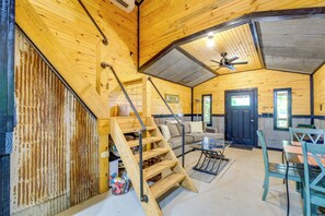 A wooden cabin interior with a staircase, a sofa, a dining table, and a ceiling fan. - Fish, Hike & Unwind! Rustic Ozark Cabin (Stella)
