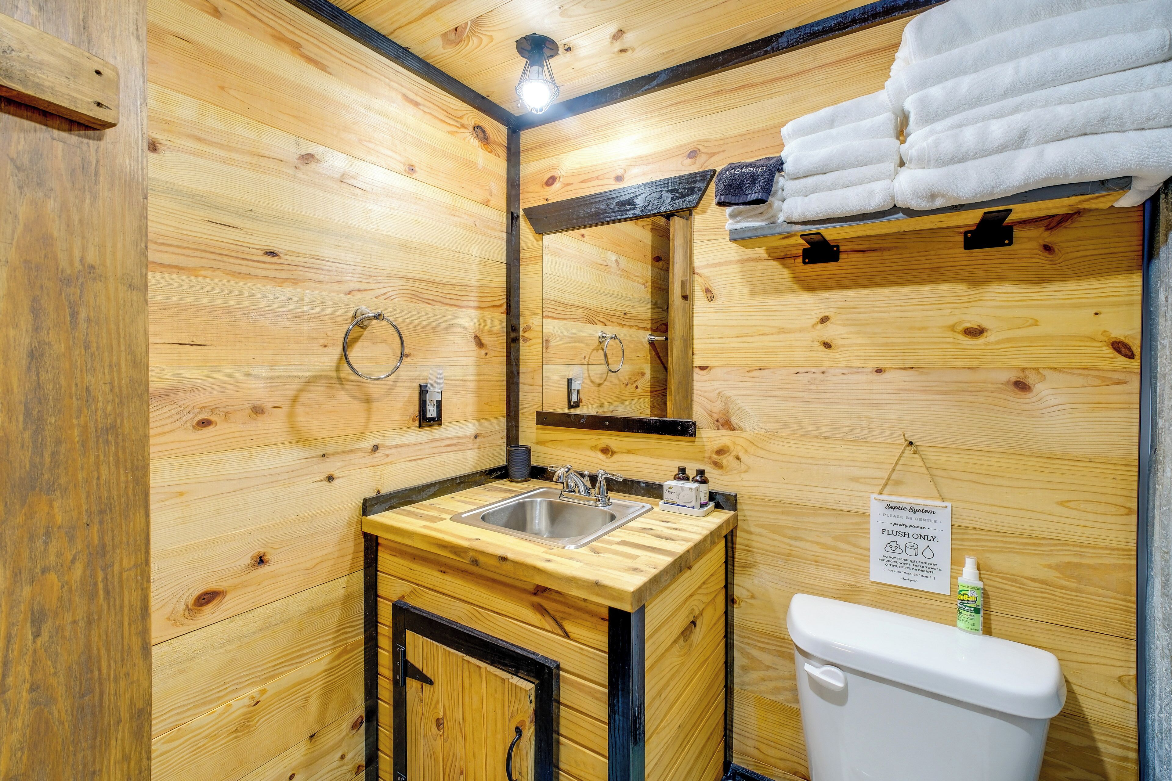 Une salle de bain de style rustique, avec des murs en bois, comprenant un lavabo, un miroir et des toilettes.