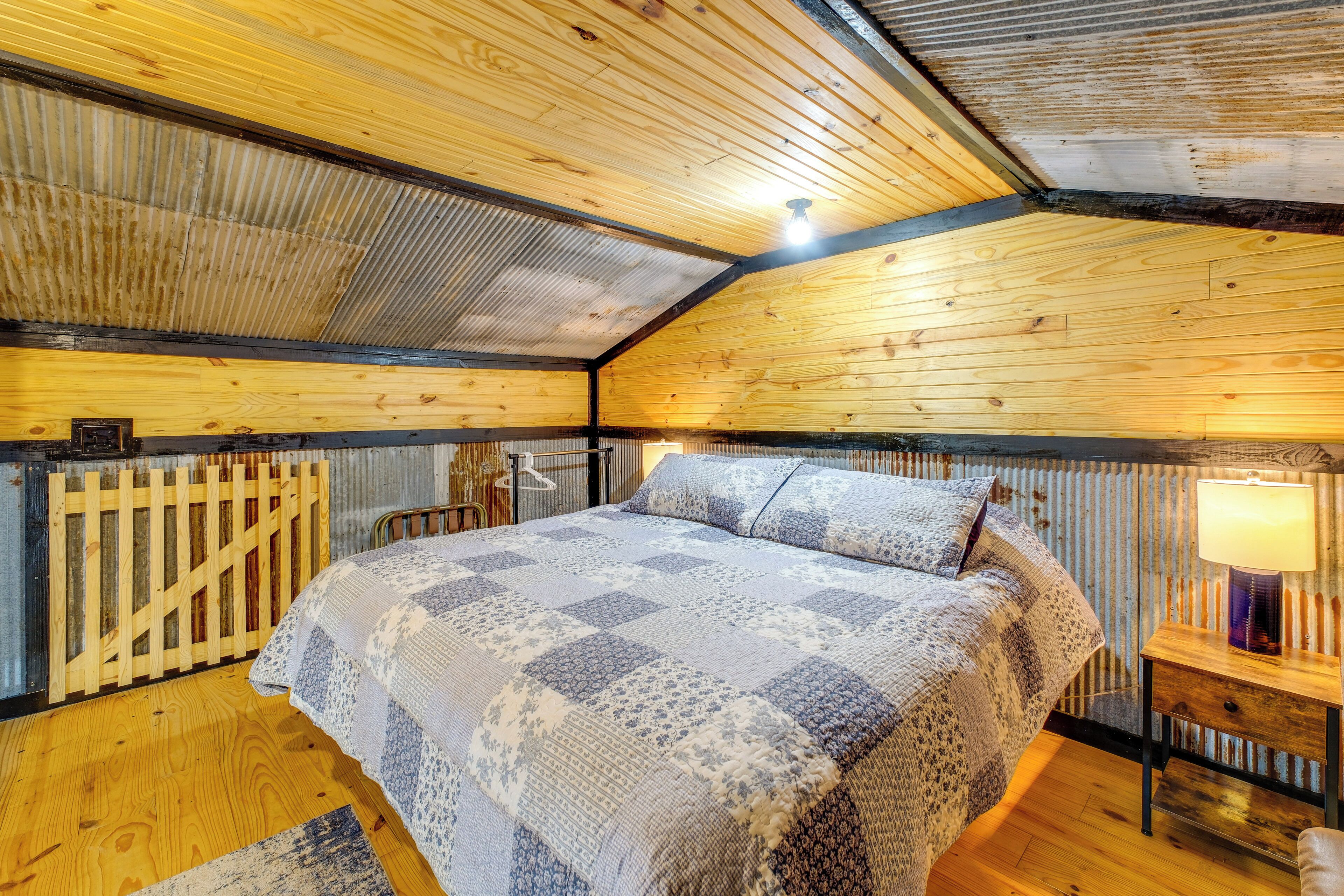 Ein gemütliches Zimmer mit Holzbalkendecke, einem Bett mit gemustertem Überwurf, einem Nachttisch mit Lampe und einem Metallgitter.