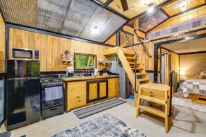 A compact kitchen with a microwave, stove, and refrigerator. A wooden staircase leads to a loft bedroom. - On-site Trails & Fishing Pond: Rustic Ozark Cabin (Stella)