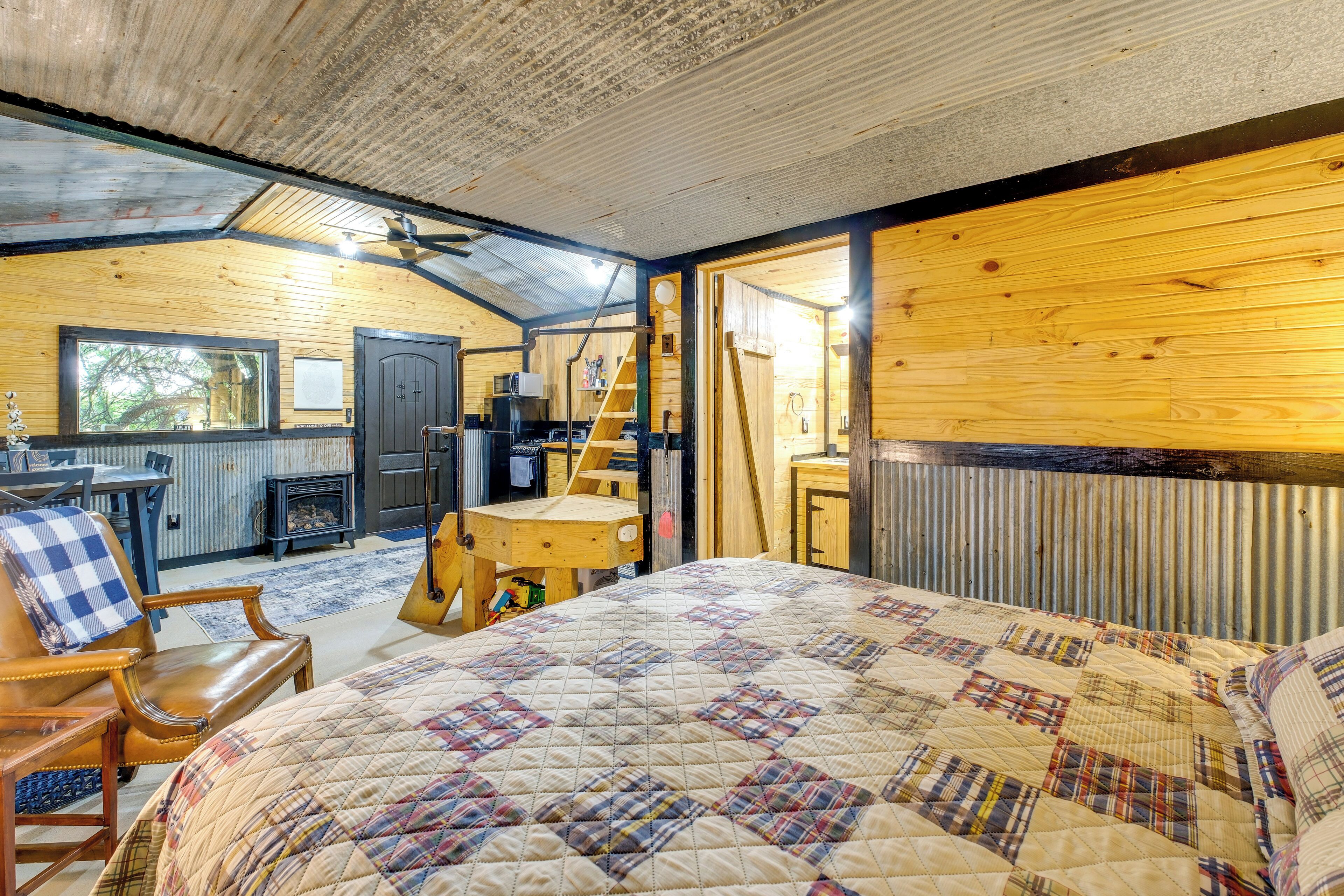 Interior acogedor de una cabaña con una cama grande, un escritorio de madera, una silla, una escalera y vistas al exterior.