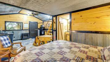 Interior acogedor de una cabaña con una cama grande, un escritorio de madera, una silla, una escalera y vistas al exterior.
