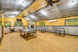 Une table de ping-pong dans une pièce aux murs en bois, dotée de ventilateurs de plafond et de fenêtres.