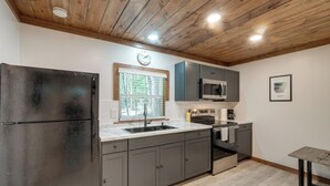 A modern kitchen with a stainless steel refrigerator, grey cabinets, a microwave, and a sink. - Woodsy Cabot Escape in Arkansas Countryside! (Cabot)