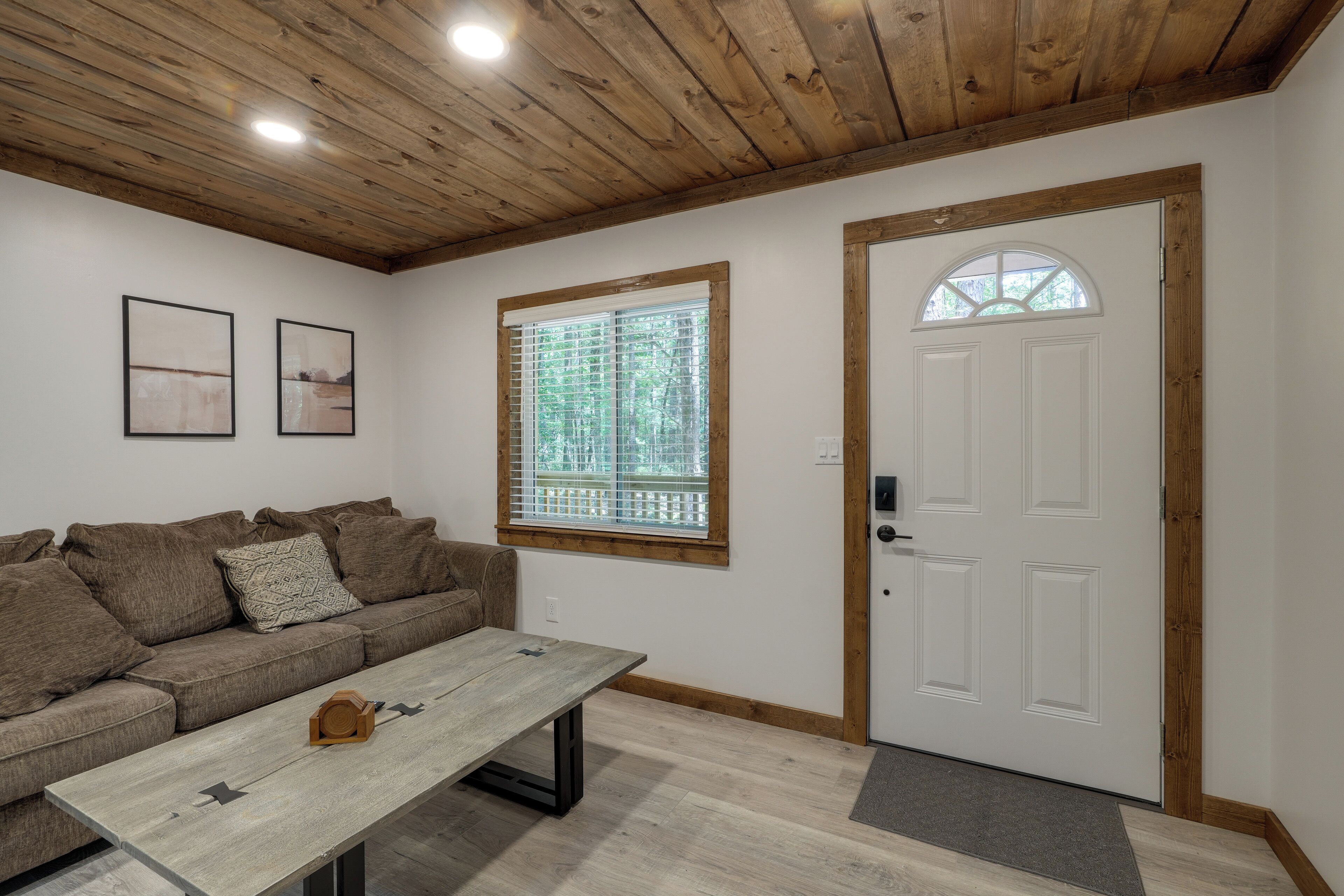 Una habitación con techo de madera, una puerta blanca con ventana, un sofá marrón y una mesa de madera.